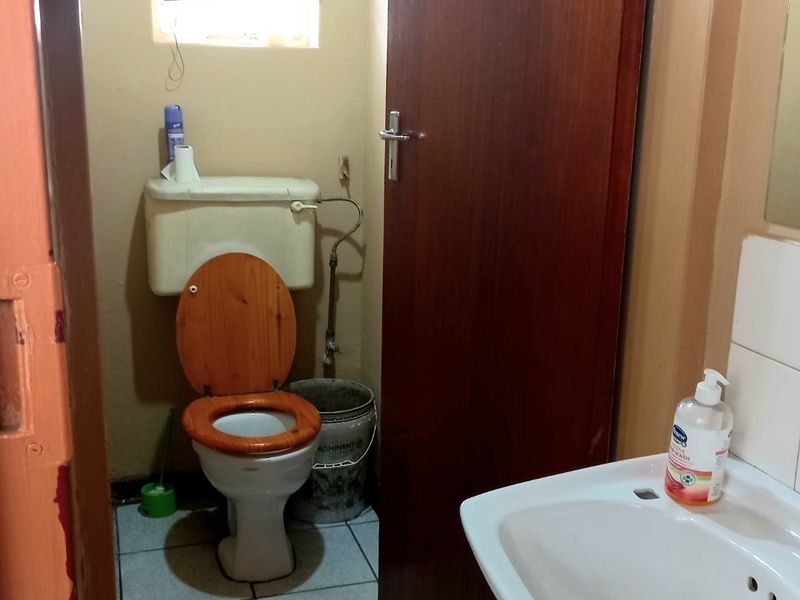 A compact bathroom featuring a standard toilet, ceramic washbasin, and tiled flooring, requiring cosmetic updates to improve its overall condition.