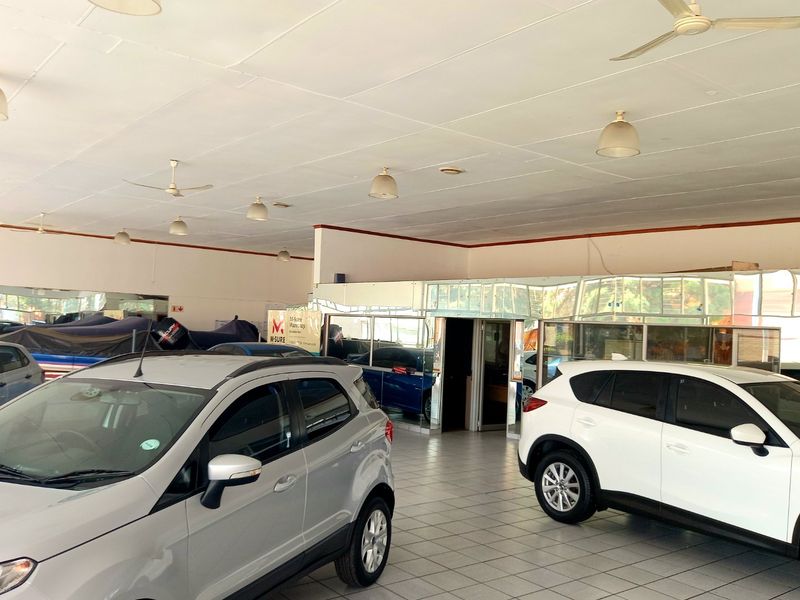 Spacious commercial showroom area featuring tiled flooring, multiple ceiling fans, and glass-partitioned office or display sections.