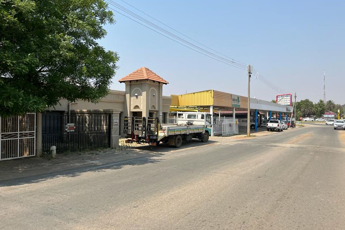 Street view of a commercial property featuring a gated entrance, perimeter wall, and an adjacent commercial structure with a metal roof.