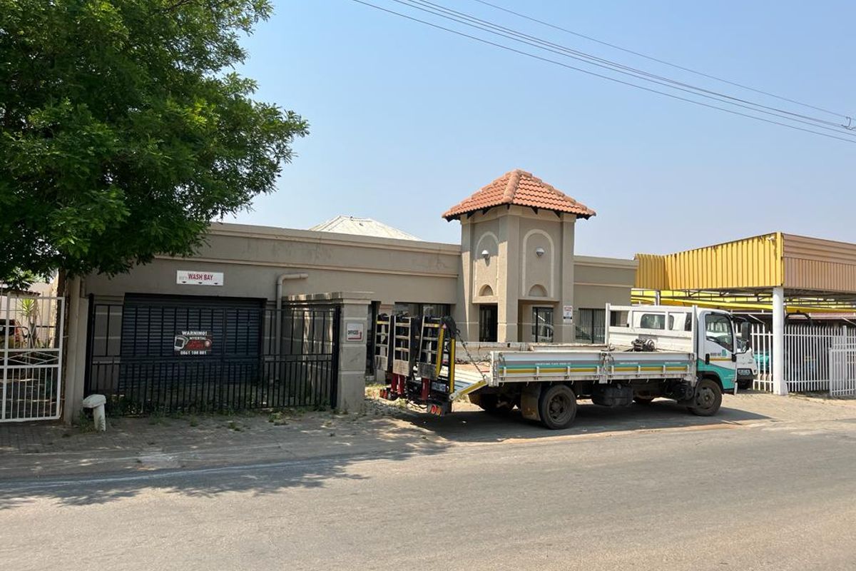 Commercial property frontage featuring a turret architectural detail, secure perimeter fencing, a roller shutter wash bay entrance, and an adjacent metal carport structure.