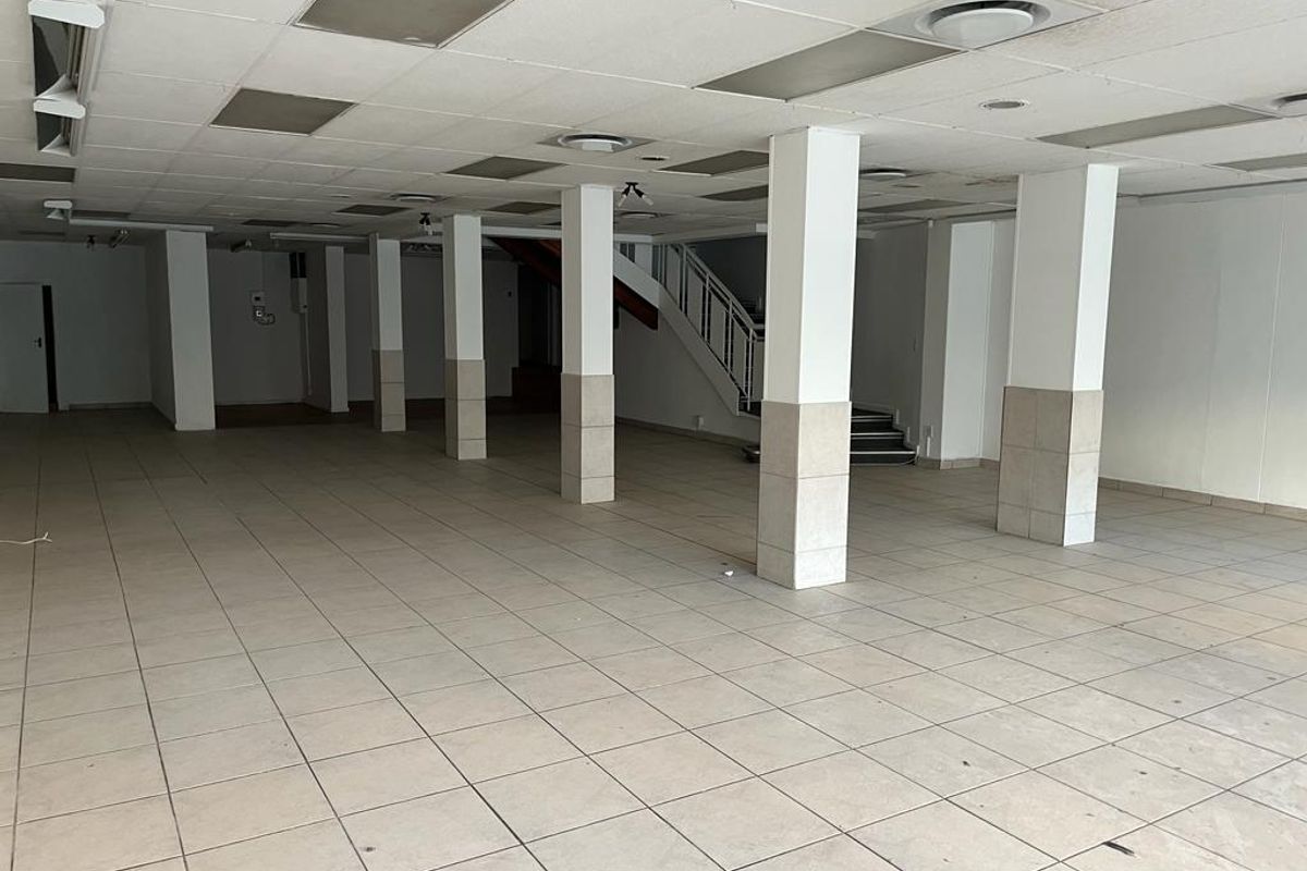 A spacious, vacant commercial open-plan area featuring tiled flooring, structural columns, and a suspended ceiling with recessed lighting and an internal staircase.