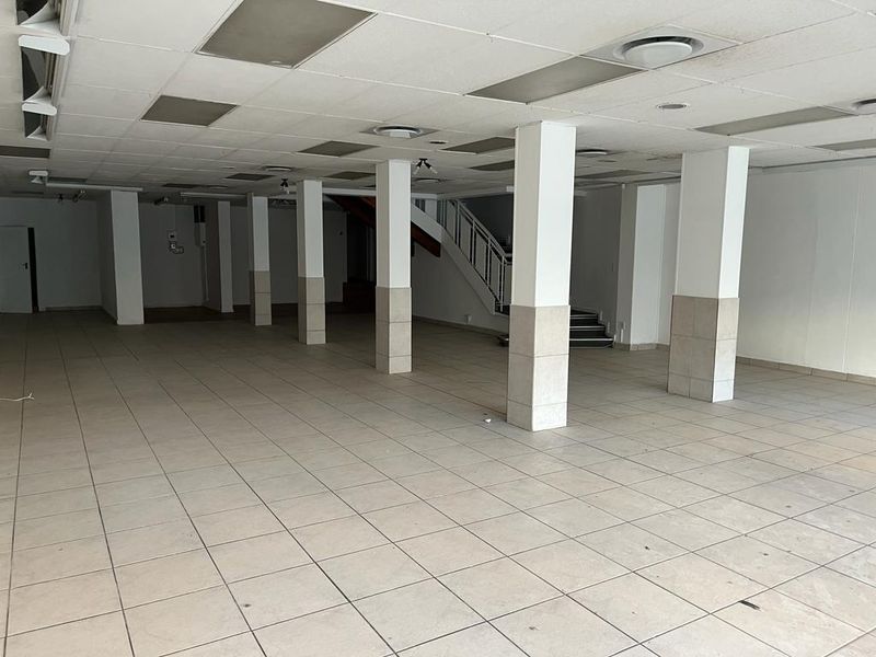 A spacious, vacant commercial open-plan area featuring tiled flooring, structural columns, and a suspended ceiling with recessed lighting and an internal staircase.