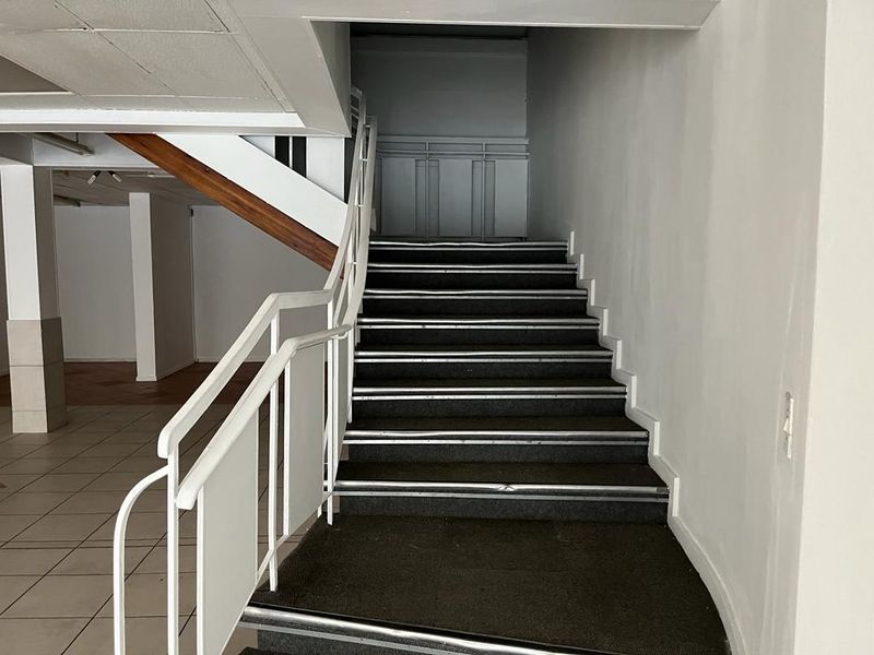 An empty commercial hallway featuring a staircase with metal handrails, carpeted treads, and tiled flooring, leading to an upper level.