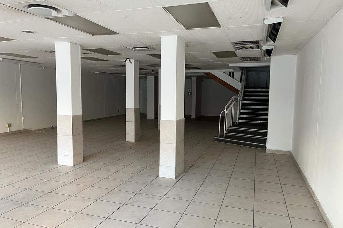A spacious, vacant commercial open-plan area featuring tiled flooring, structural columns, a suspended ceiling with recessed lighting, and an internal staircase.