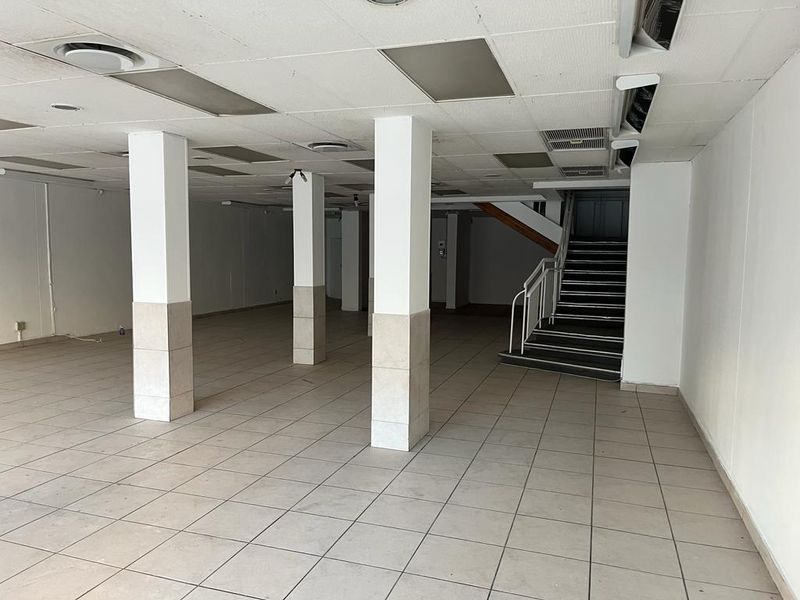 A spacious, vacant commercial open-plan area featuring tiled flooring, structural columns, a suspended ceiling with recessed lighting, and an internal staircase.