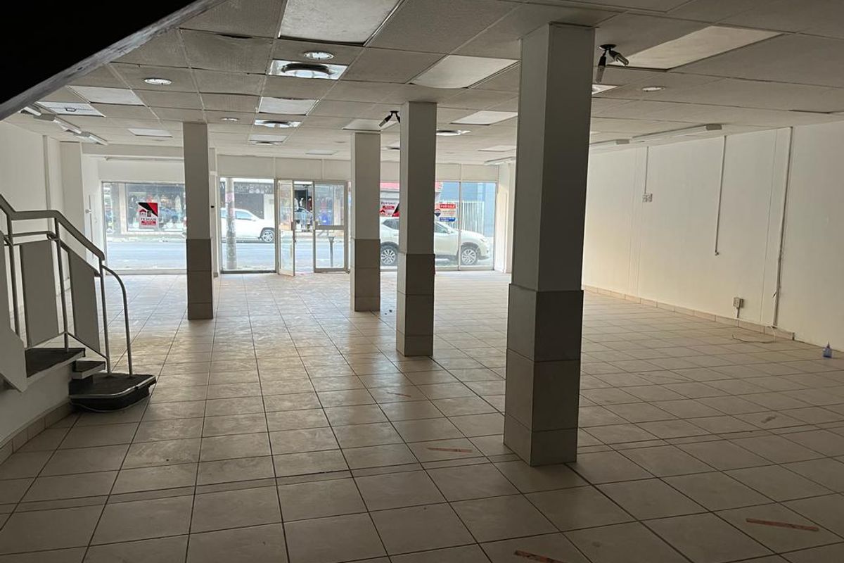 Spacious open-plan commercial retail space featuring ceramic tile flooring, structural support columns, a suspended ceiling, and large glass storefront windows for high visibility.