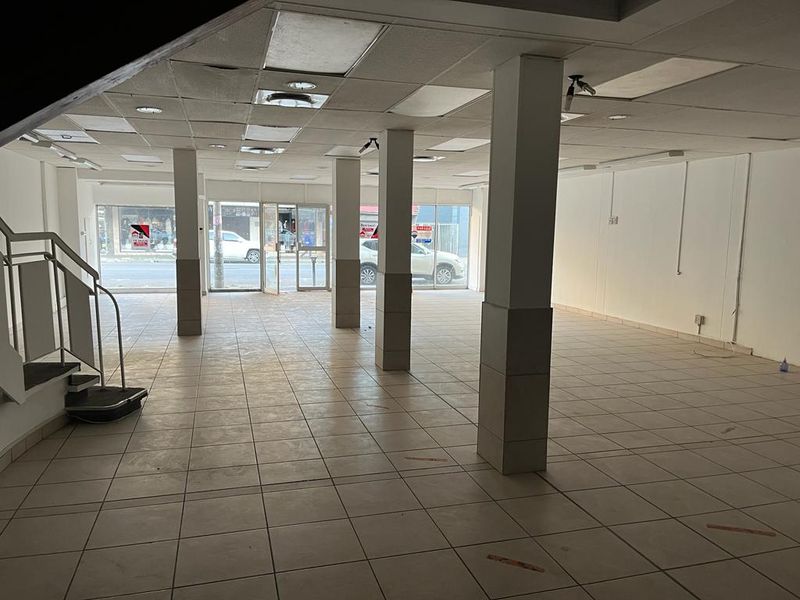 Spacious open-plan commercial retail space featuring ceramic tile flooring, structural support columns, a suspended ceiling, and large glass storefront windows for high visibility.