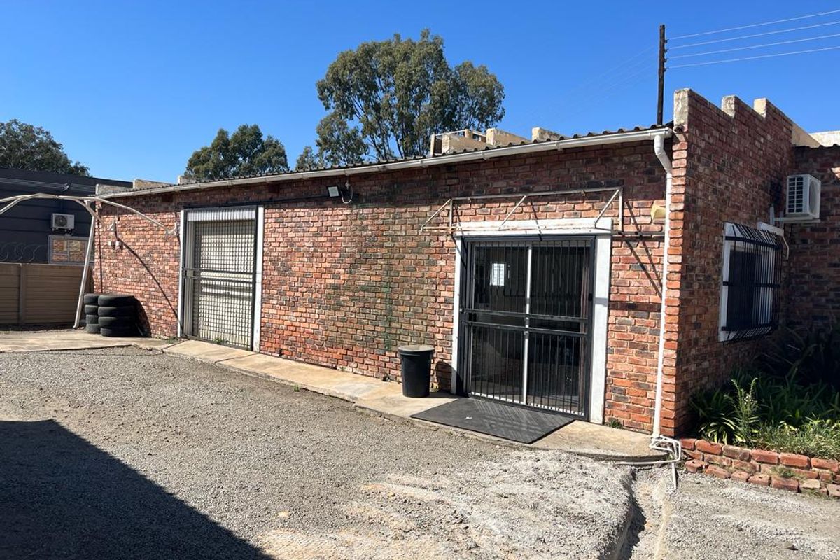 Rear view of a commercial face brick building featuring security gates, window bars, and an external air conditioning unit with a gravel yard area.