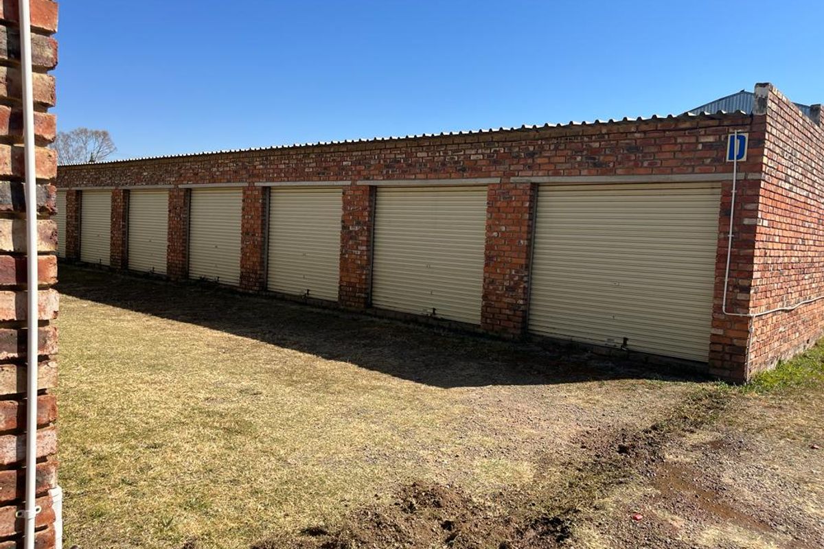 A row of six commercial storage garage units featuring brick construction and cream-colored roller shutter doors.