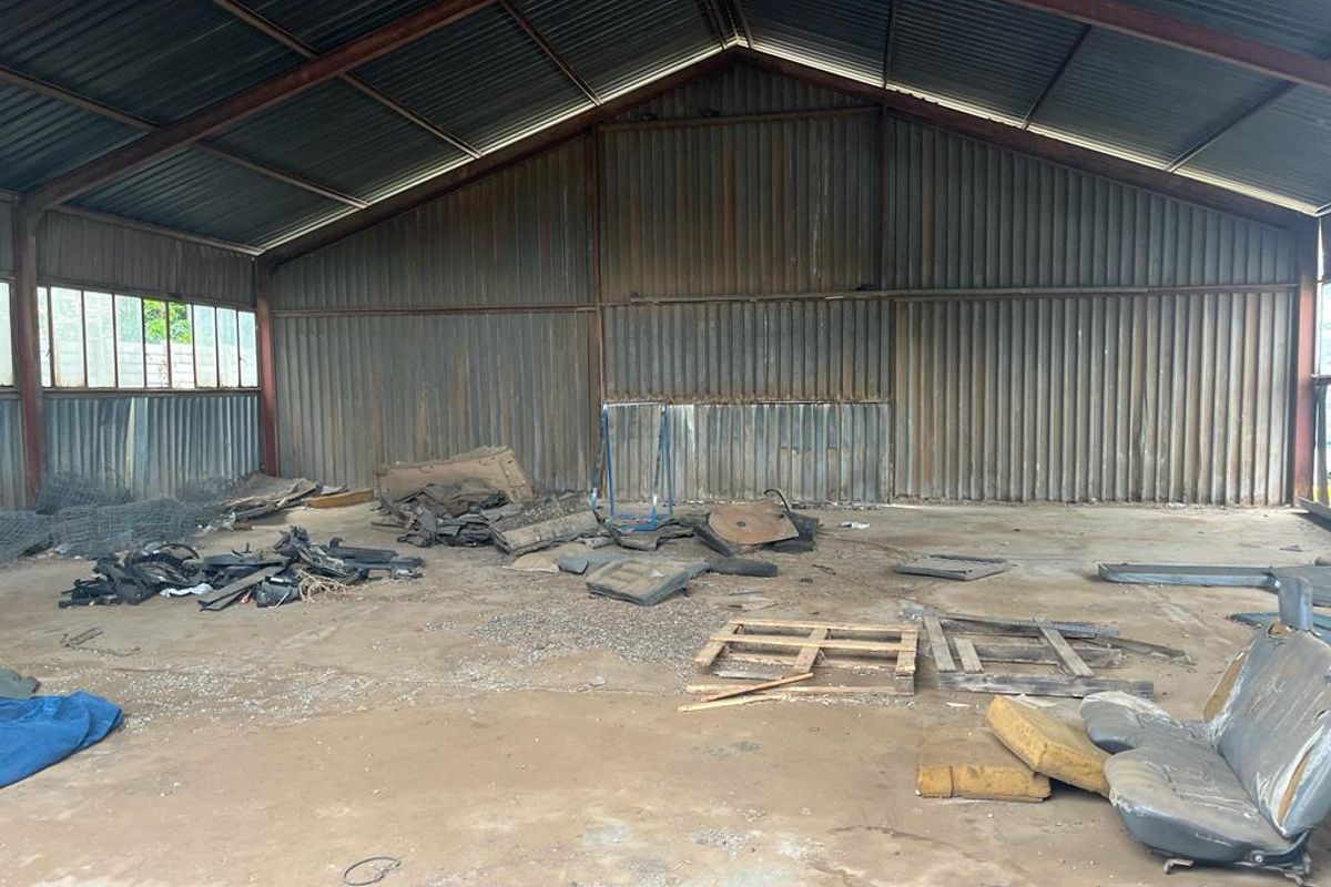 Large industrial utility space featuring corrugated metal walls, exposed steel roof trusses, and concrete flooring, suitable for storage or workshop conversion.