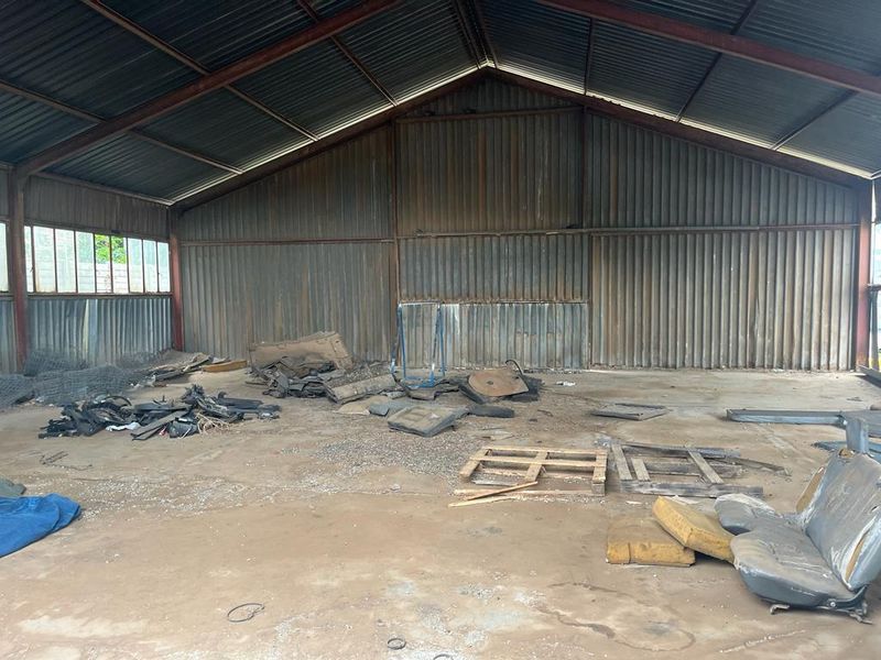 Large industrial utility space featuring corrugated metal walls, exposed steel roof trusses, and concrete flooring, suitable for storage or workshop conversion.