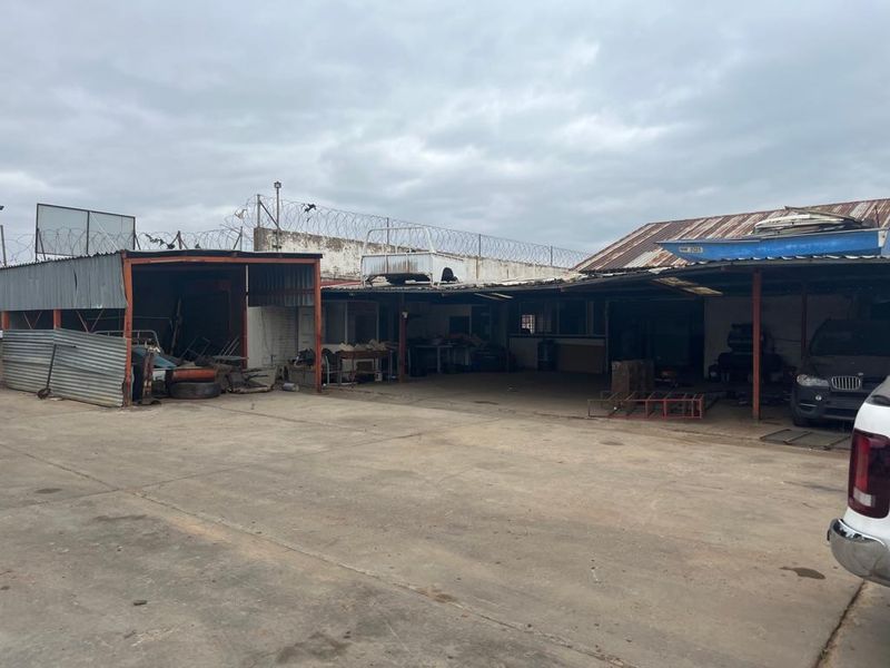 Commercial yard area featuring open-sided storage bays with corrugated metal roofing, concrete flooring, and perimeter security fencing.