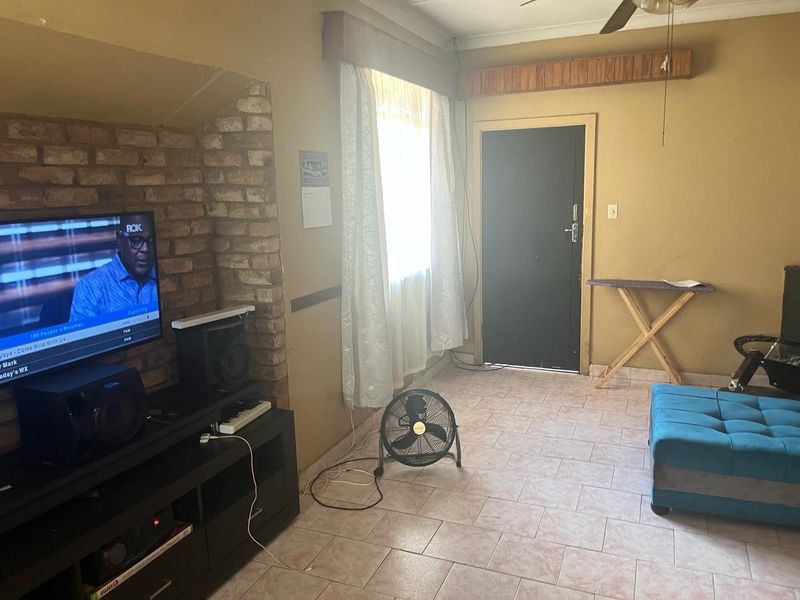 Living room featuring an exposed brick accent wall, tiled flooring, and a ceiling fan, offering a functional space with potential for cosmetic updates.