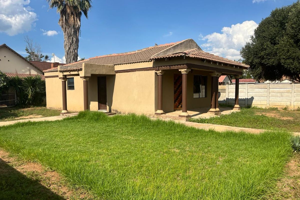 Rear view of a single-story house featuring a covered patio with decorative columns, a tiled roof, and a large surrounding garden area.