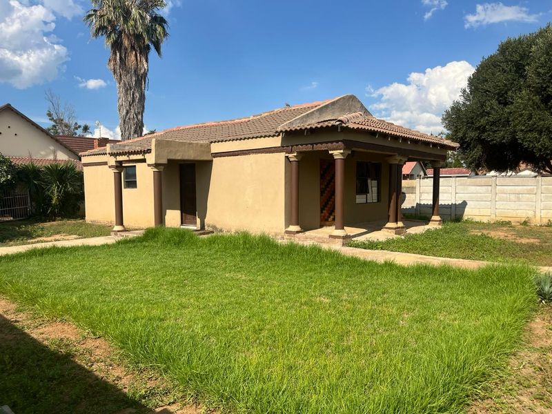 Rear view of a single-story house featuring a covered patio with decorative columns, a tiled roof, and a large surrounding garden area.