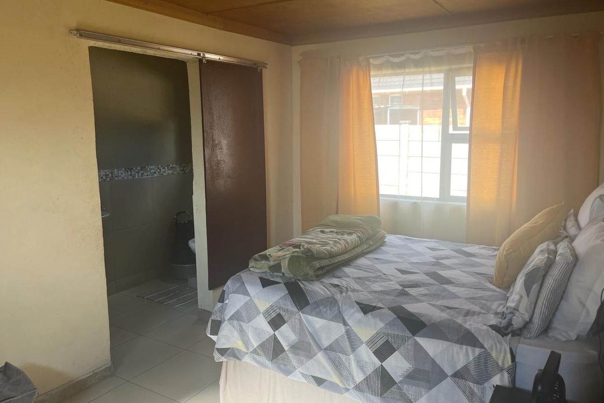 A bedroom featuring tiled flooring, a sliding door leading to an en-suite bathroom, and natural light from the window.