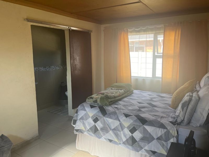 A bedroom featuring tiled flooring, a sliding door leading to an en-suite bathroom, and natural light from the window.