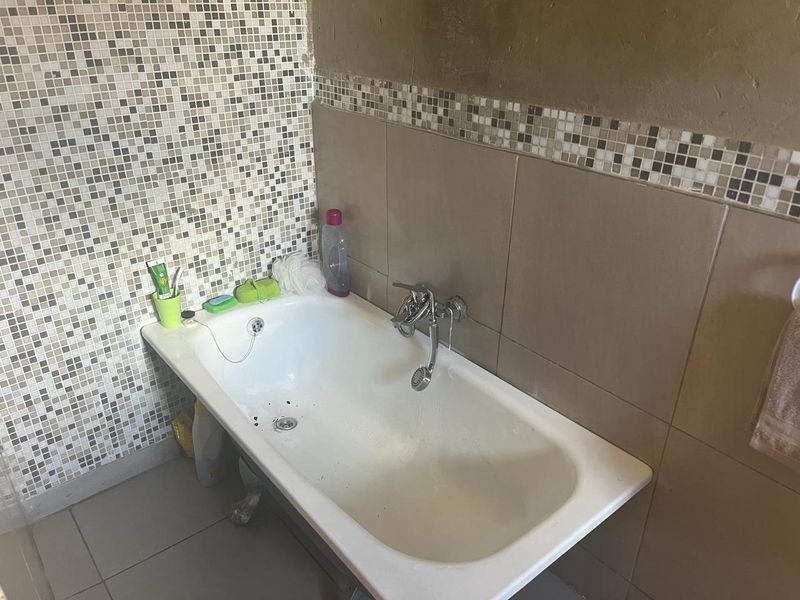 A bathroom featuring a bathtub with a wall-mounted mixer tap and handheld shower head, finished with mosaic and ceramic wall tiling.