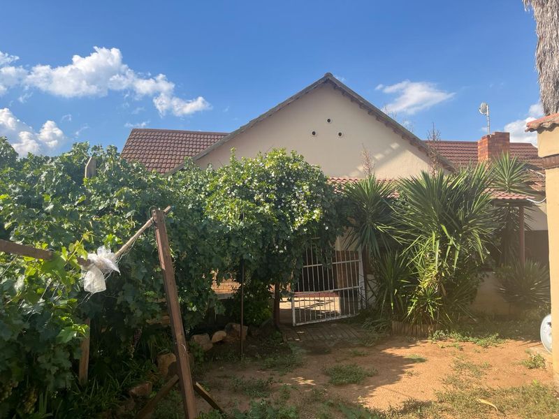 Rear view of the property featuring a tiled roof, brick chimney, and a paved patio area accessed through a metal security gate.