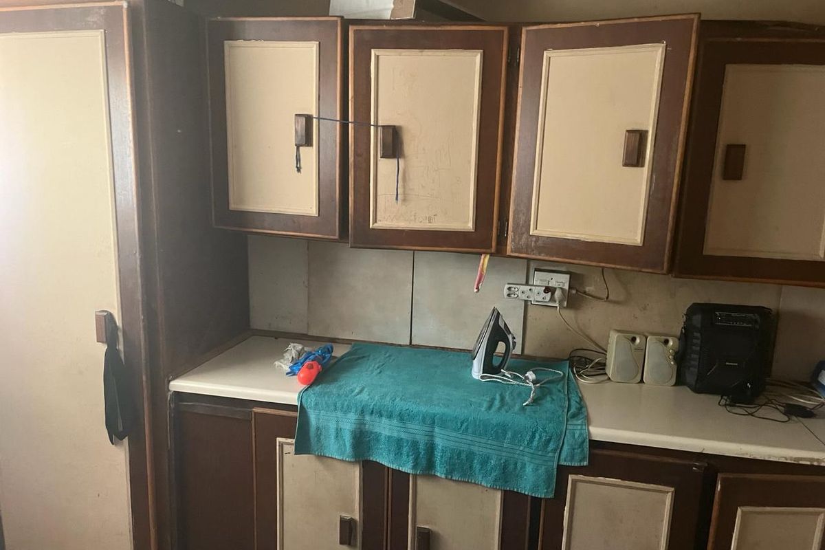 A dated kitchen area featuring worn built-in cabinetry, laminate countertops, and tiled backsplash, offering significant potential for modernization and renovation.