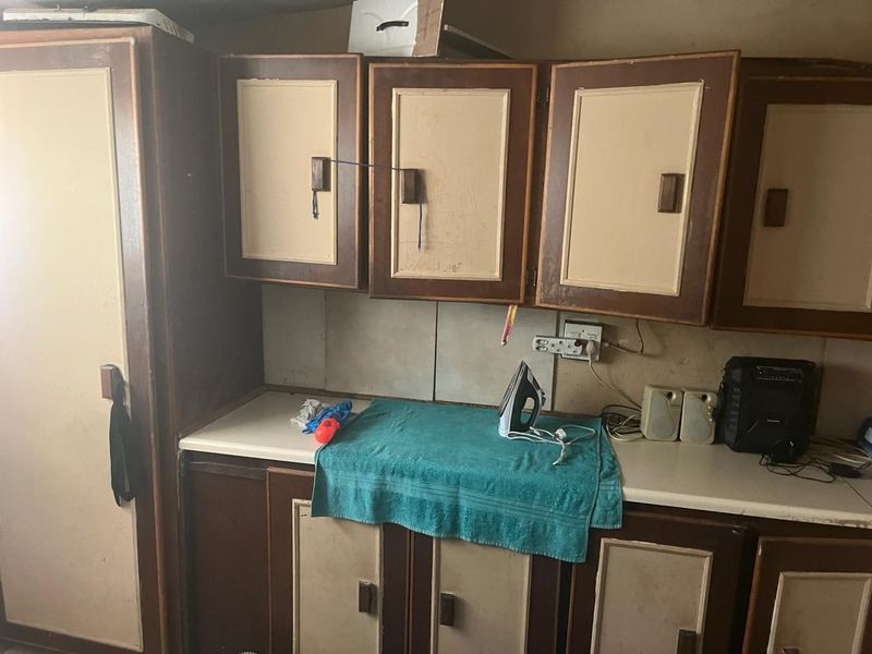 A dated kitchen area featuring worn built-in cabinetry, laminate countertops, and tiled backsplash, offering significant potential for modernization and renovation.