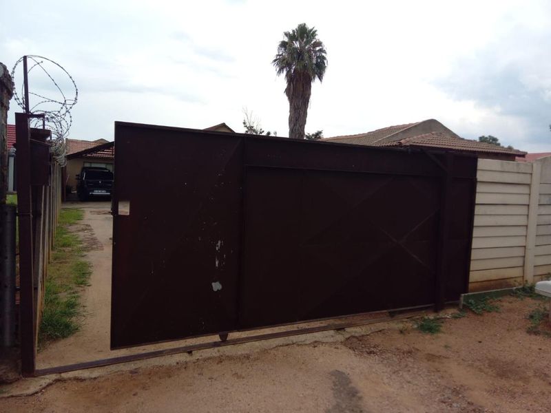 Front entrance view featuring a sliding metal gate with security razor wire and a precast concrete boundary wall.