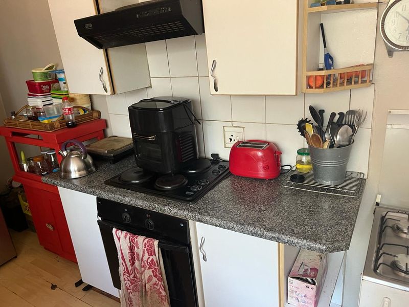 A compact kitchen area featuring a built-in oven, electric hob, extractor fan, and tiled splashback with laminate cabinetry and granite-look countertops.