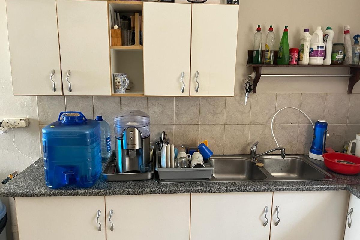 A functional kitchen area featuring double stainless steel sinks, laminate countertops, tiled backsplash, and ample upper and lower cabinetry for storage.