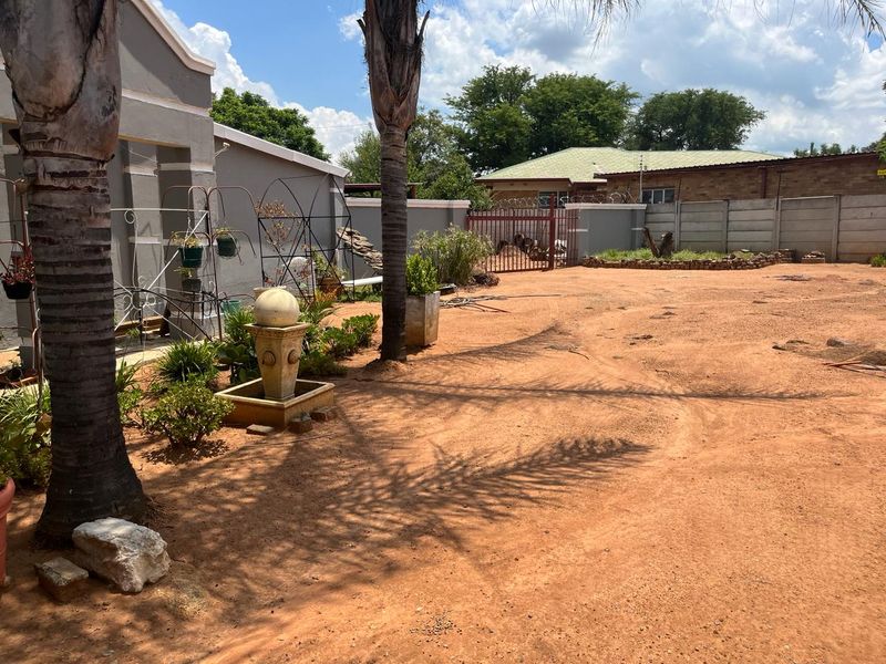 A spacious rear yard featuring a large sandy area, perimeter precast concrete walling with security fencing, and established palm trees.