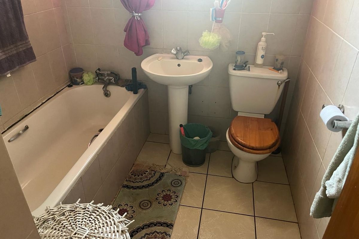 A compact bathroom featuring a pedestal basin, bathtub, and toilet with tiled walls and flooring, offering potential for modernization.