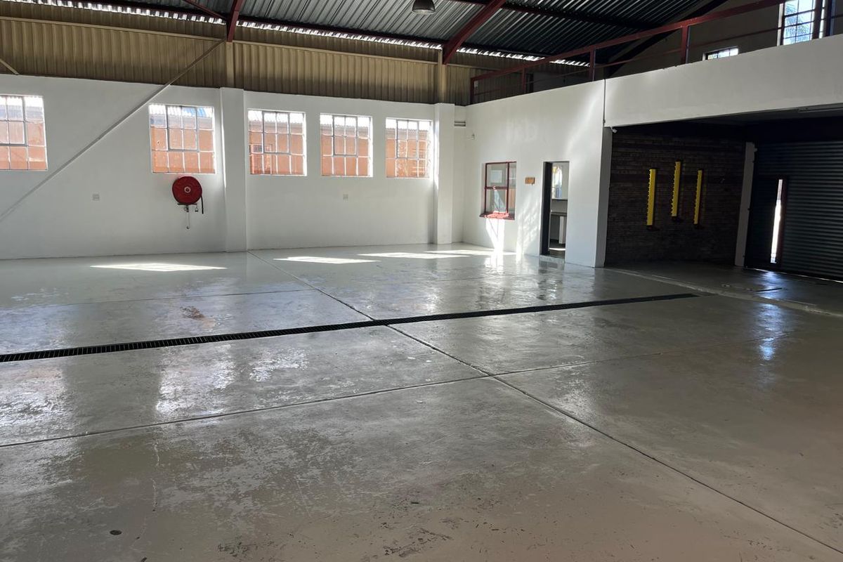 Spacious industrial utility area featuring polished epoxy flooring, high ceilings with exposed steel trusses, and a mezzanine level, suitable for workshop or storage use.