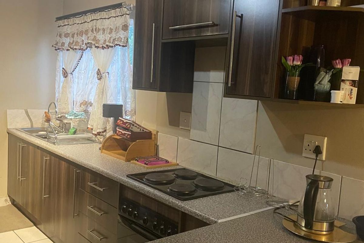 A functional kitchen featuring dark wood-look cabinetry, a built-in electric hob and oven, tiled splashbacks, and a breakfast bar counter.