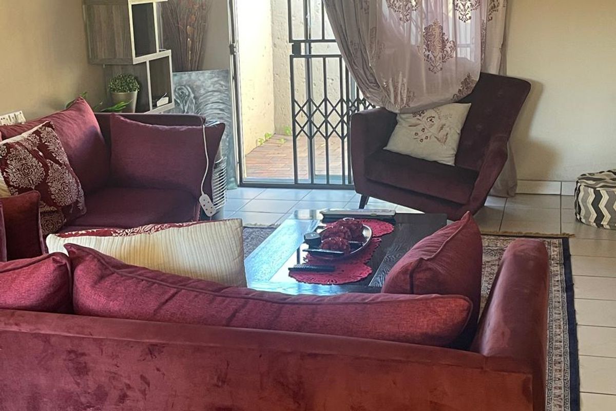 A comfortable living room featuring tiled flooring and a sliding glass door with security gate providing access to the outdoor area.