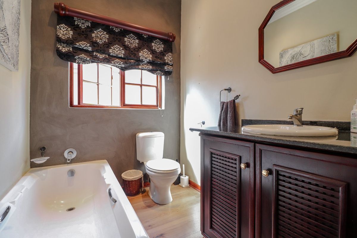 A functional bathroom featuring a built-in bathtub, a dark wood vanity with a stone countertop, and a toilet.