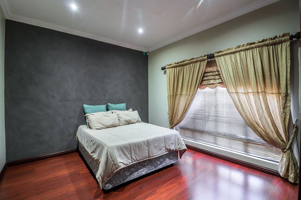 A well-maintained bedroom featuring dark wood-look flooring, a textured accent wall, and recessed ceiling lighting.