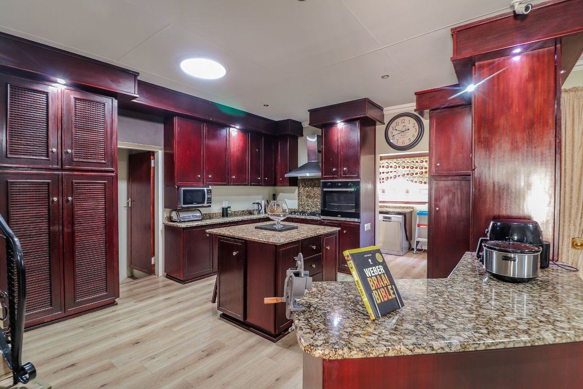 Spacious kitchen featuring dark wood cabinetry, granite countertops, a central island, built-in oven, and extractor fan.