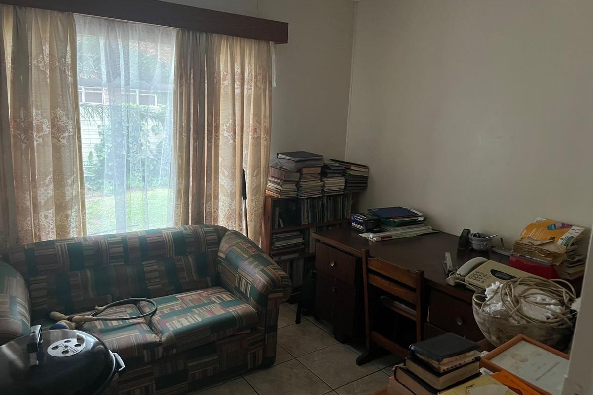 A bedroom featuring tiled flooring and a window with a curtain pelmet, currently utilized as a home office and storage space.