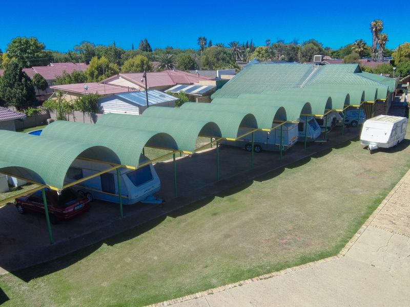 Aerial view of a commercial property featuring a long, covered corrugated metal carport structure providing parking for multiple vehicles and caravans.
