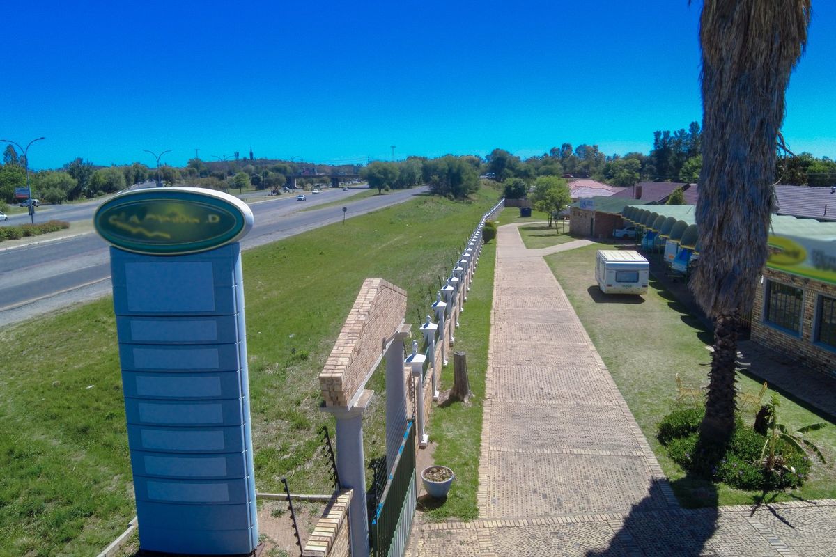 Aerial view of the commercial property exterior, featuring a paved walkway, boundary wall, and prominent signage pylon adjacent to the main road.