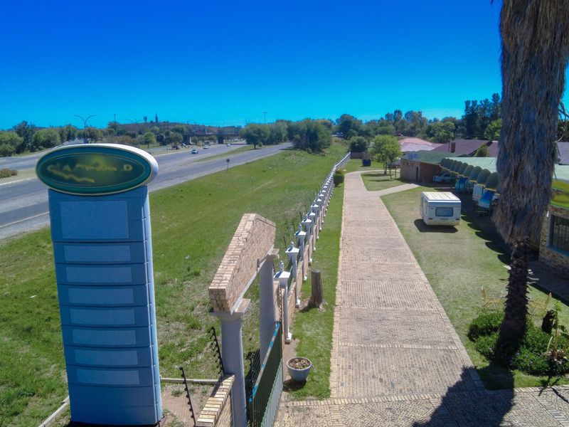 Aerial view of the commercial property exterior, featuring a paved walkway, boundary wall, and prominent signage pylon adjacent to the main road.