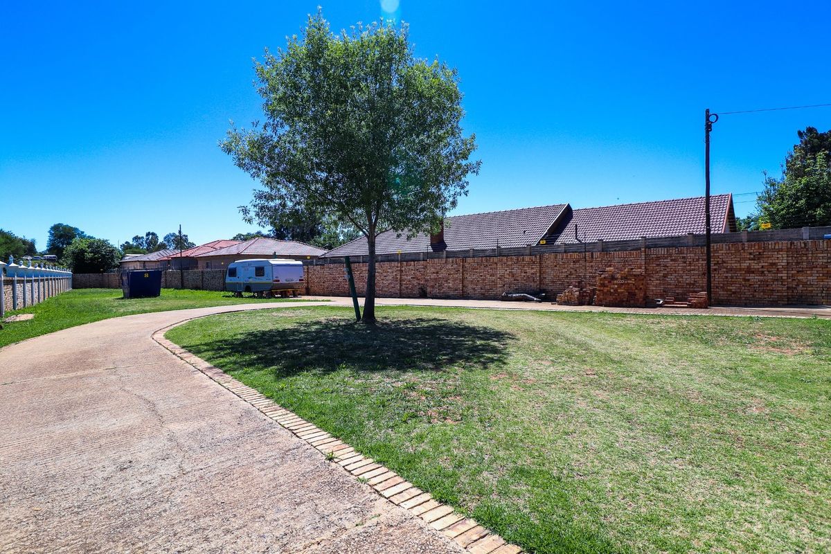 Spacious rear yard featuring a concrete driveway, expansive lawn area, and secure brick boundary walling with electric fencing.
