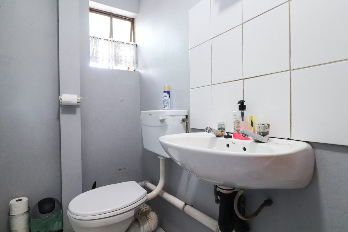 A compact bathroom featuring a wall-mounted ceramic basin, a standard toilet, and white wall tiling, requiring minor cosmetic updates to improve its overall appearance.
