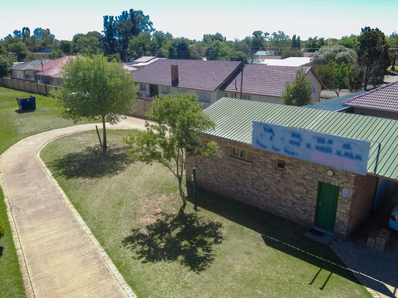 Aerial view of a commercial property featuring a brick building with a pitched metal roof, paved driveway, and perimeter wall.