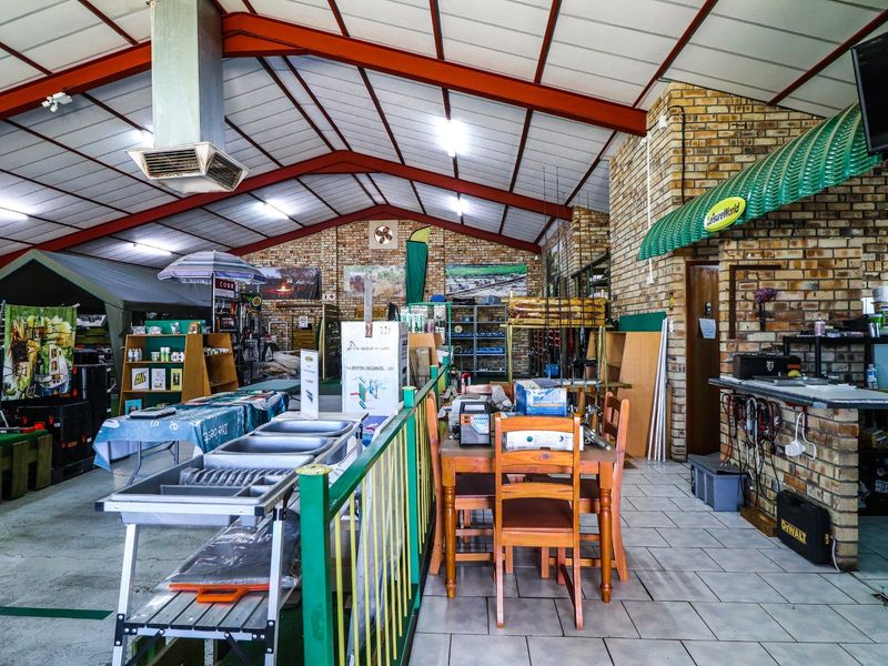 Spacious commercial open-plan retail area featuring exposed steel roof trusses, brick wall accents, and durable tiled flooring with integrated utility sink.