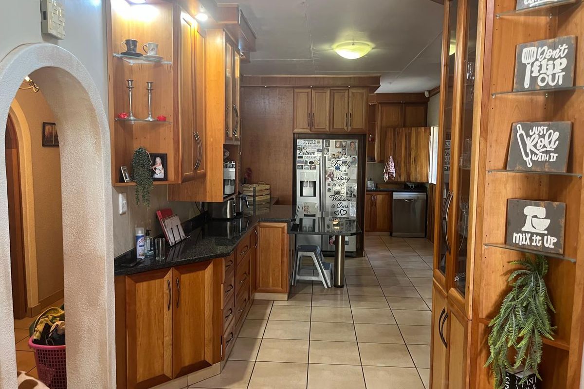 A spacious kitchen featuring extensive wooden cabinetry, granite countertops, and tiled flooring, connected to an adjacent area through a classic arched doorway.