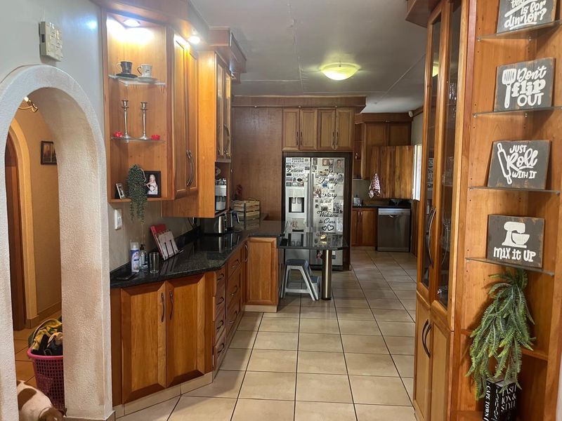 A spacious kitchen featuring extensive wooden cabinetry, granite countertops, and tiled flooring, connected to an adjacent area through a classic arched doorway.