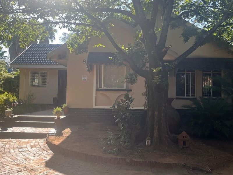 Front elevation of a single-story house featuring a brick paved driveway, mature tree, and security bars on the windows.