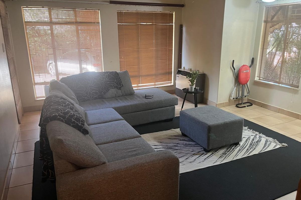 A living room featuring tiled flooring, large windows with venetian blinds, and a built-in gas heater.