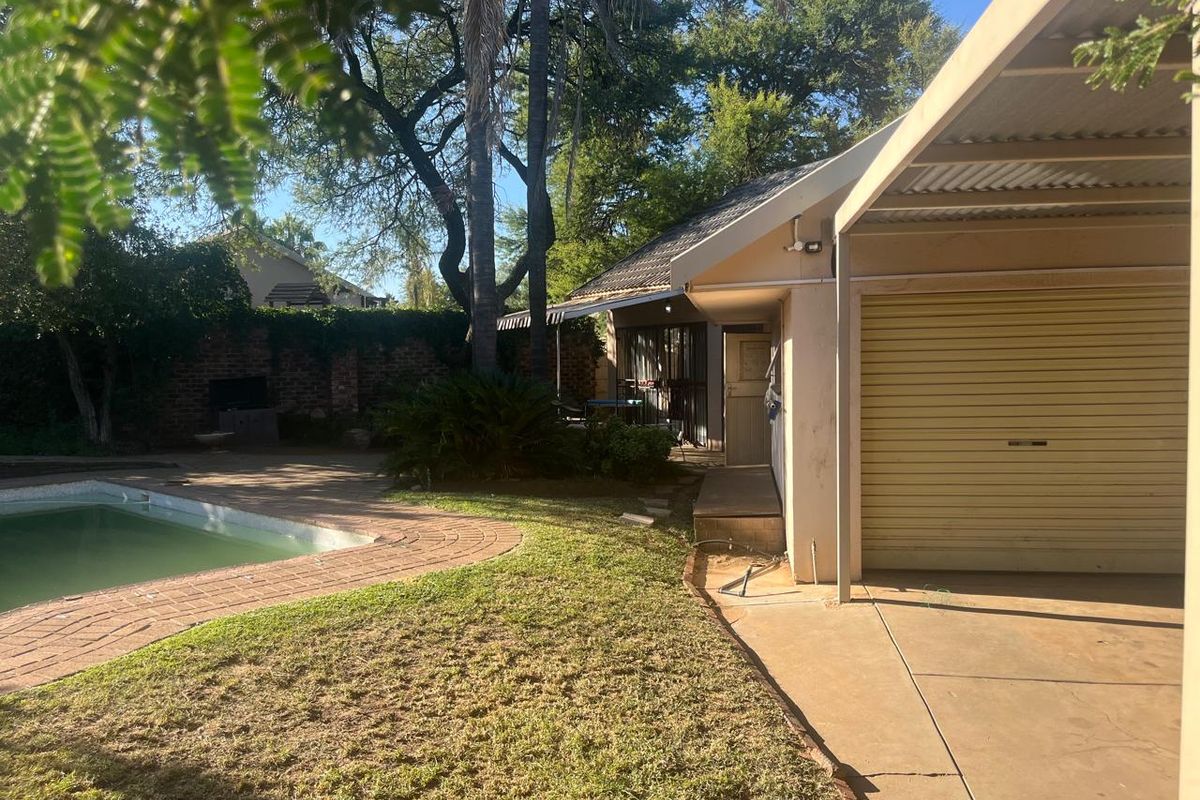 Rear garden area featuring a swimming pool, brick paving, a built-in braai, and a garage with an attached carport.