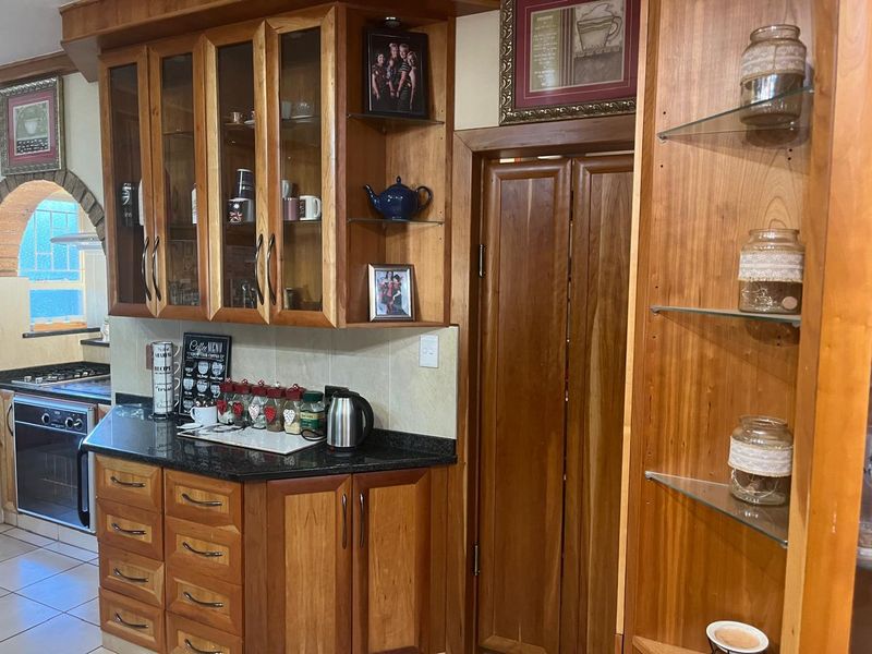 A traditional kitchen featuring warm wooden cabinetry, granite countertops, built-in oven, gas hob, and glass display shelving.